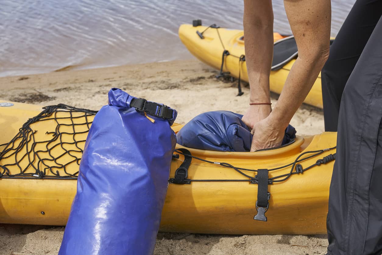 Female hiker puts a waterproof dry bag into the kayak